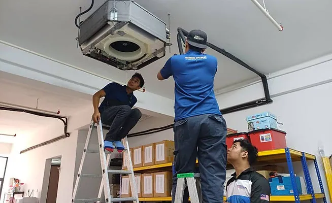 Technicians servicing a ceiling cassette air-conditioner from a ladder