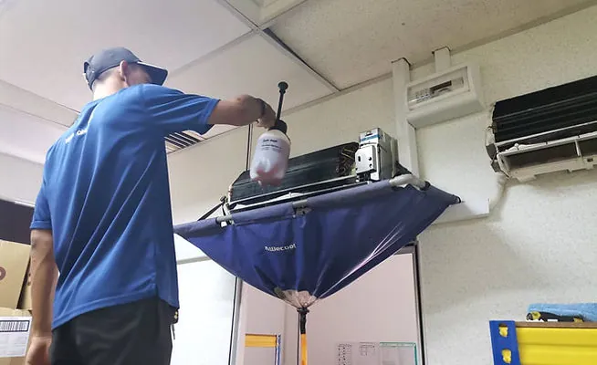 Technician cleaning an air-conditioner with a water-catching cover